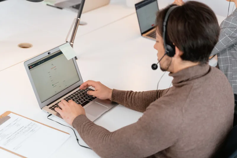 Person wearing a headset typing on a laptop at a support desk, handling live chat