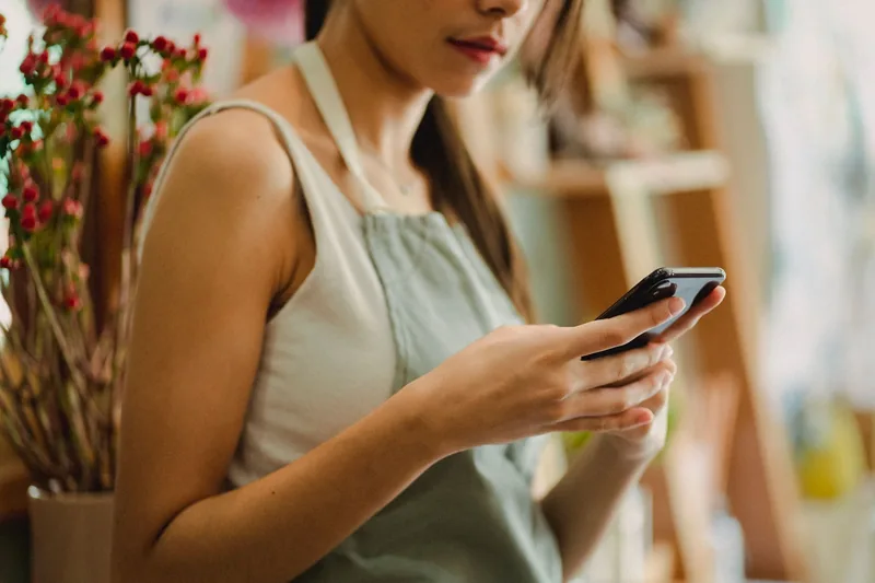 Shop owner in an apron replying to a message on her phone between customers