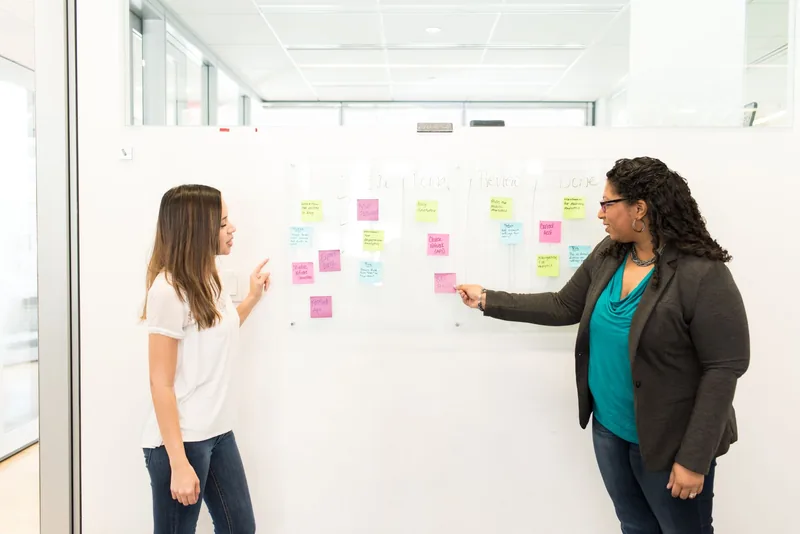 Two colleagues mapping a pipeline of sticky notes across a whiteboard