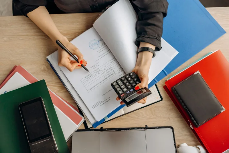 Small-business owner reviewing software costs with a calculator and documents