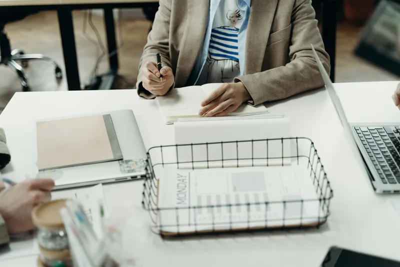 Business owner writing next week's plan in a notebook beside a laptop and a weekly planner tray