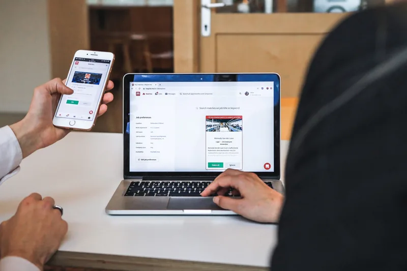 Person checking a website on a smartphone next to a laptop