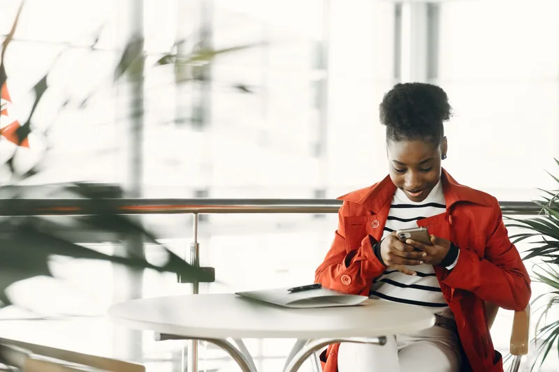 Young woman at a cafe table reading a follow-up message on her phone